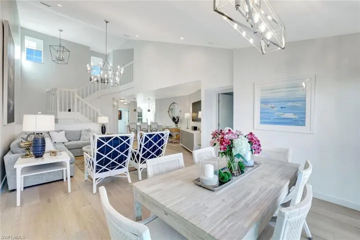 Dining room featuring stairway, light wood finished floors, a chandelier, and high vaulted ceiling