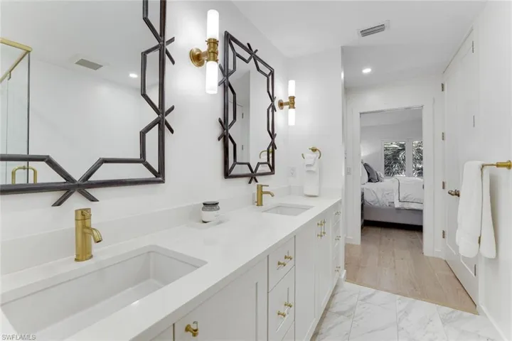 Full bathroom with double vanity, light marble finish flooring, recessed lighting, and connected bathroom