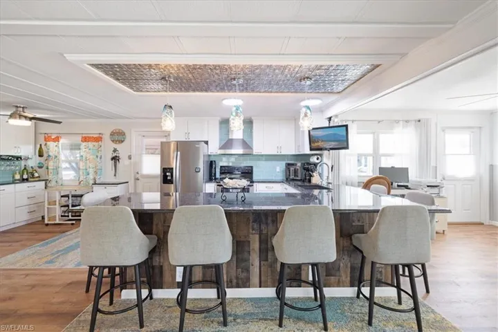 Kitchen with light wood-style flooring, decorative backsplash, stove, stainless steel refrigerator with ice dispenser, and wall chimney range hood