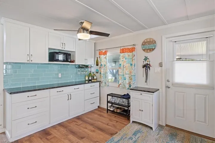 Kitchen with backsplash, black microwave, light wood-style floors, white cabinets, and a ceiling fan