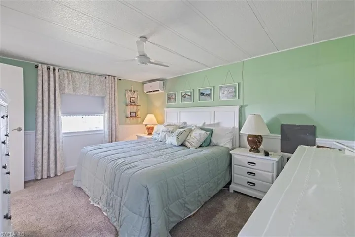 Bedroom with a textured ceiling, a ceiling fan, a wall mounted air conditioner, wainscoting, and carpet flooring