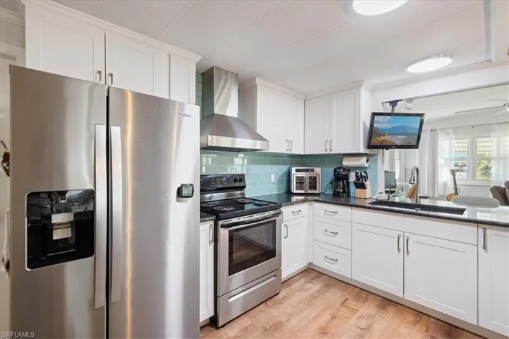 Kitchen featuring white cabinetry, stainless steel appliances, wall chimney range hood, and a sink
