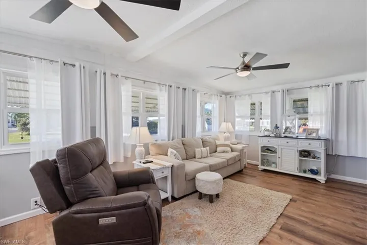 Living area with beam ceiling, baseboards, ceiling fan, and wood finished floors