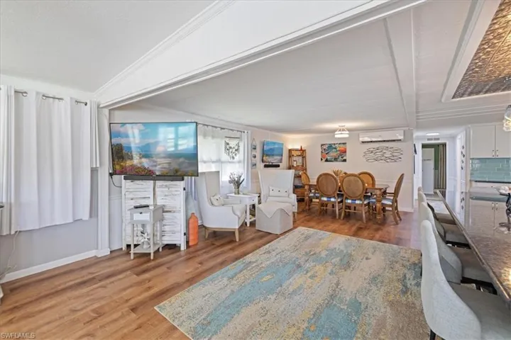 Living area with baseboards, crown molding, a wall unit AC, and wood finished floors