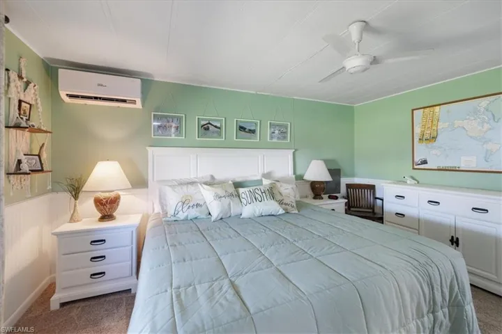 Bedroom with carpet flooring, a wall mounted air conditioner, ceiling fan, and a wainscoted wall