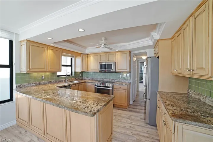 Kitchen featuring light hardwood / wood-style floors, kitchen peninsula, light stone countertops, light brown cabinets, and appliances with stainless steel finishes