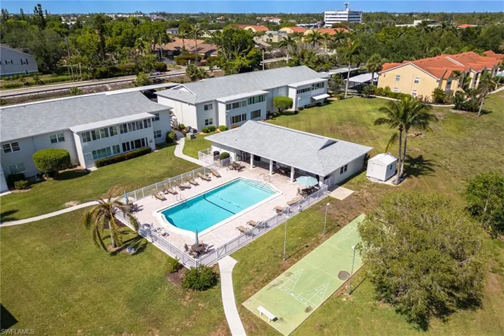 Community swimming pool with surrounding lounge area, covered patio, shuffleboard court, and manicured green spaces