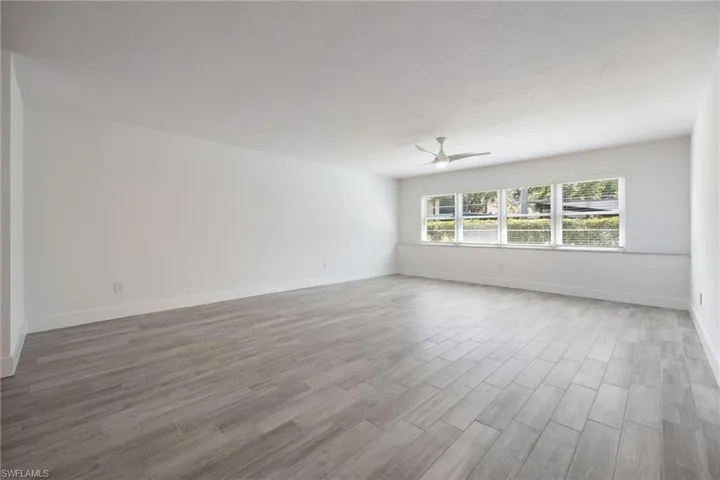 Spacious room featuring light-toned wood-look tile flooring, white walls, and multiple windows providing natural light