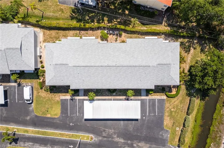 Multi-unit building featuring a gray shingle roof, paved parking areas, and mature landscaping