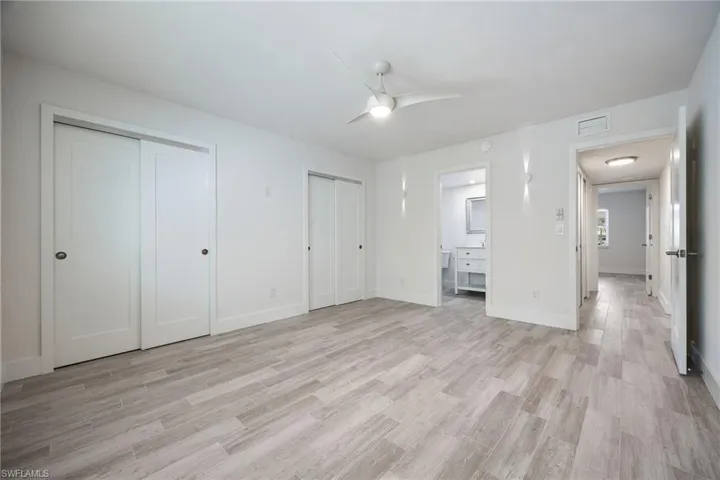 Spacious room featuring light wood-finish flooring, white walls, and a modern ceiling fan