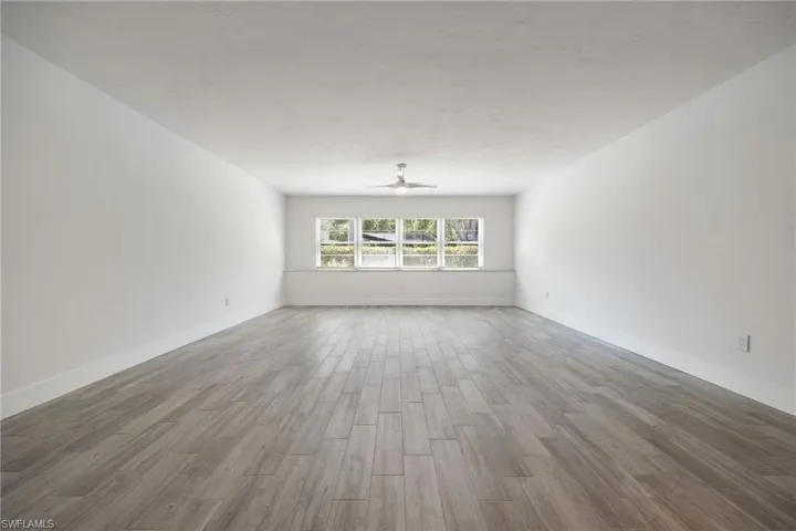Spacious interior room featuring wood-finish flooring, white baseboards, and a modern ceiling fan