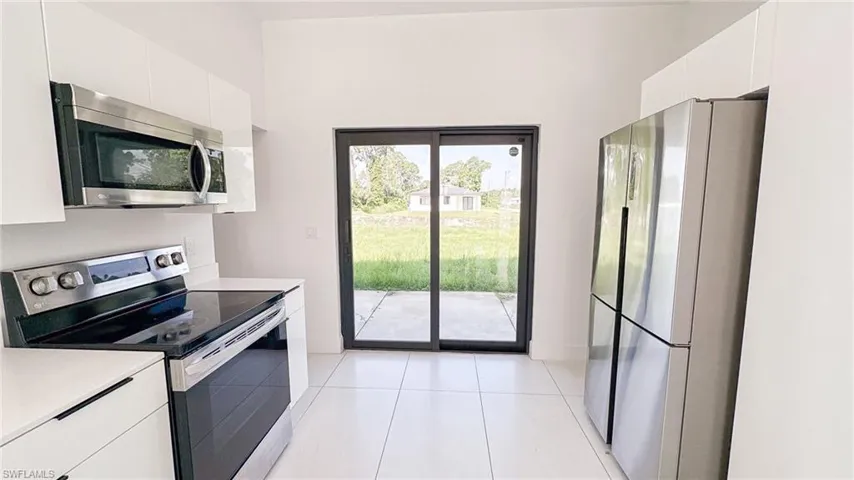 Modern kitchen featuring white cabinetry, stainless steel appliances, white tile flooring, and sliding glass doors to the exterior