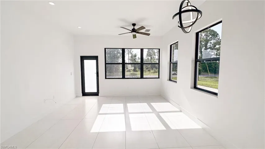 Spacious room featuring white tile flooring, white walls, and multiple large windows with black frames