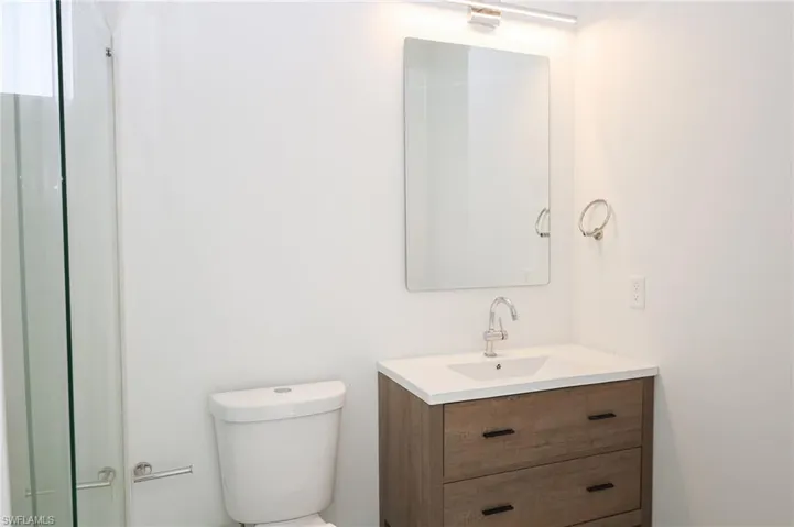 Bathroom featuring a wood-finish vanity with a white countertop and integrated sink, a rectangular mirror, and an overhead vanity light