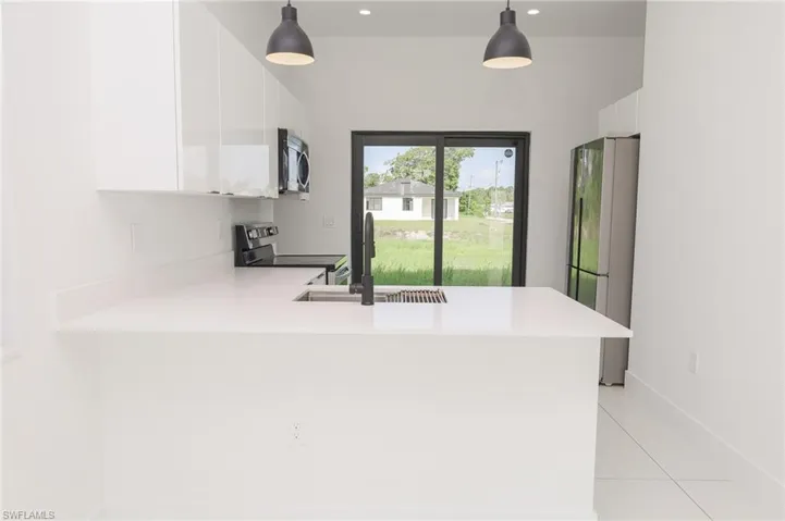 Modern kitchen featuring white cabinetry, light countertops, stainless steel appliances, and a matte black faucet