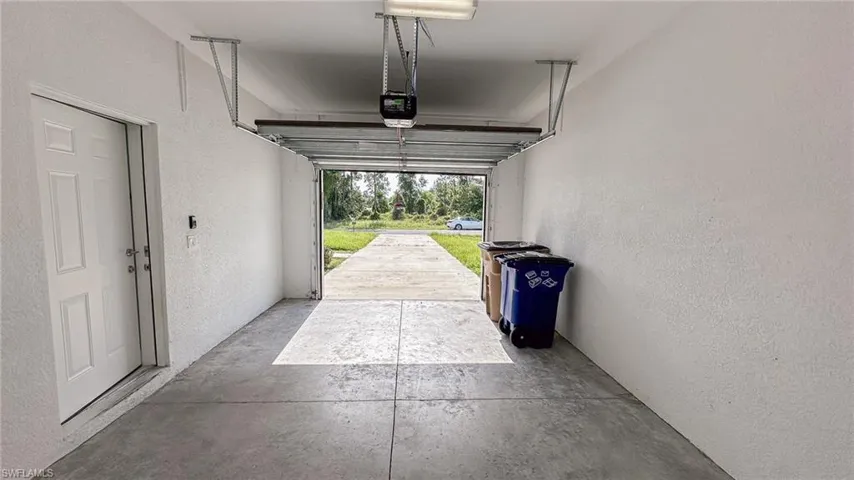 Single-car garage featuring a concrete floor, textured white walls, and an overhead garage door opener