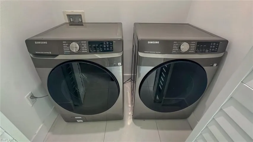 Dedicated laundry area featuring a front-load washer and dryer set, white tile flooring, and clean white walls