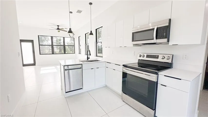 Modern kitchen featuring white cabinetry, stainless steel appliances, a center island with sink, and white tile flooring