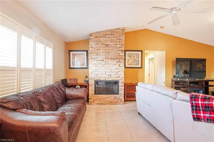 Living room featuring lofted ceiling, a stone fireplace, light tile patterned floors, and a ceiling fan