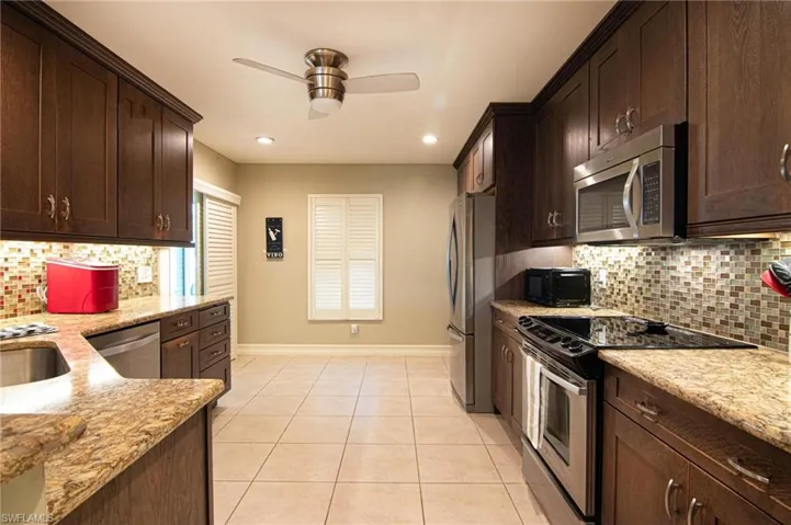 Kitchen featuring decorative backsplash, stainless steel appliances, dark brown cabinets, light stone countertops, and recessed lighting