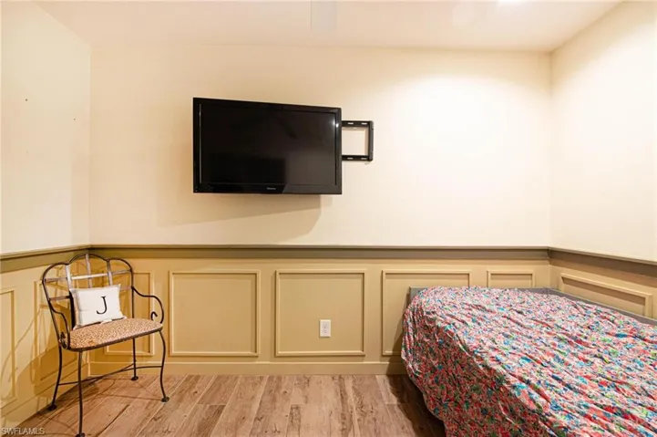 Bedroom with a decorative wall, wainscoting, light wood-style floors, and a ceiling fan