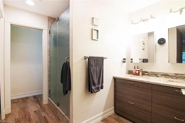 Full bath featuring double vanity, dark wood-style floors, a shower stall, and tasteful backsplash