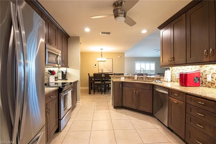 Kitchen featuring backsplash, stainless steel appliances, dark brown cabinets, light stone counters, and a peninsula