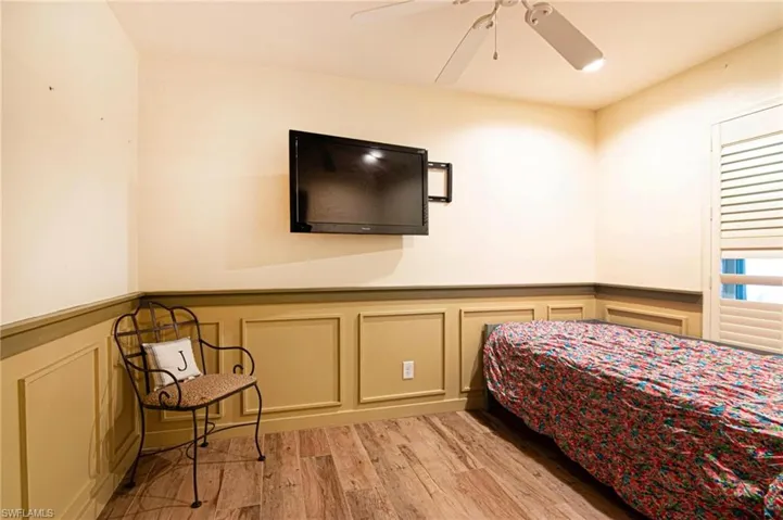 Bedroom featuring a decorative wall, a wainscoted wall, light wood-style flooring, and ceiling fan