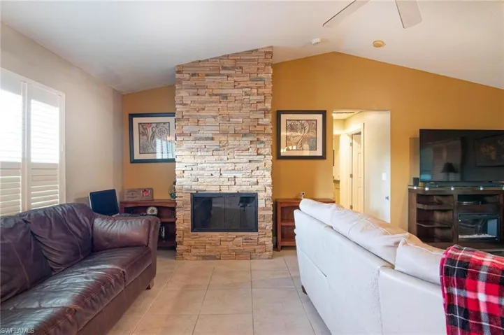 Living room with a stone fireplace, tile patterned flooring, ceiling fan, and lofted ceiling