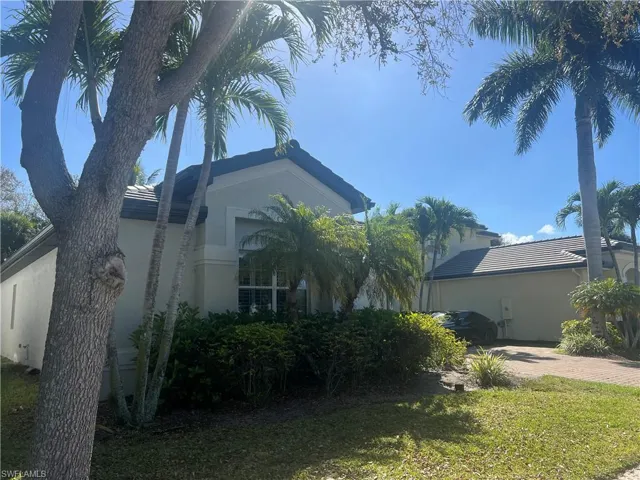 View of side of property featuring a tile roof, stucco siding, decorative driveway, and a lawn