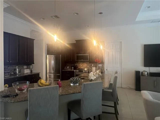 Kitchen featuring ornamental molding, stainless steel appliances, backsplash, a kitchen breakfast bar, and light stone counters