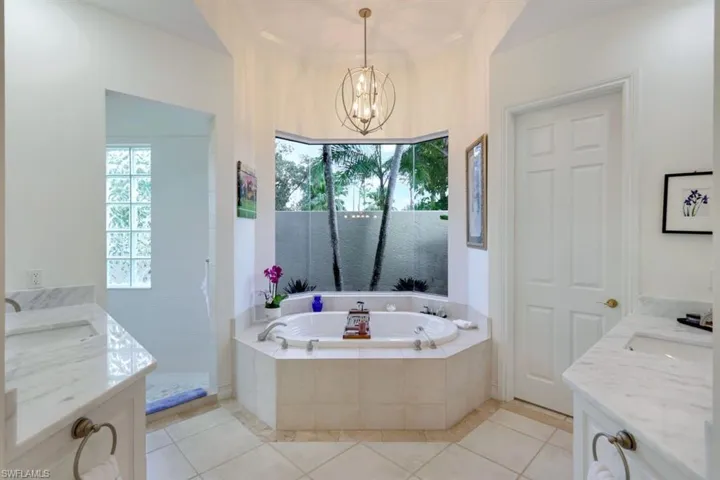 Bathroom with vanity, a notable chandelier, tiled bath, and tile patterned flooring