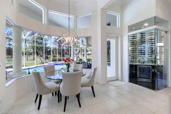 Tiled dining area with crown molding, a notable chandelier, a towering ceiling, and beverage cooler