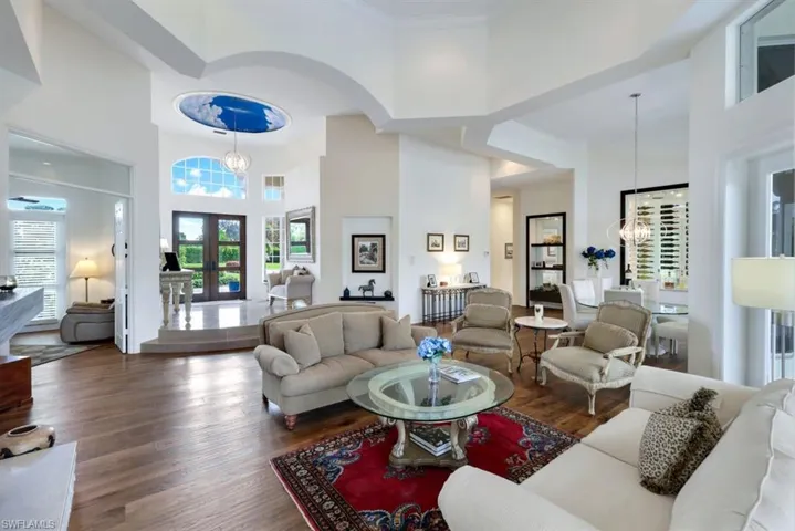 Living room featuring french doors, ornamental molding, an inviting chandelier, a towering ceiling, and dark hardwood / wood-style flooring
