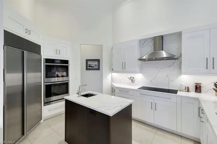 Kitchen featuring wall chimney range hood, appliances with stainless steel finishes, and white cabinets