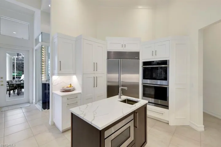 Kitchen featuring white cabinets, a kitchen island with sink, built in appliances, and a high ceiling