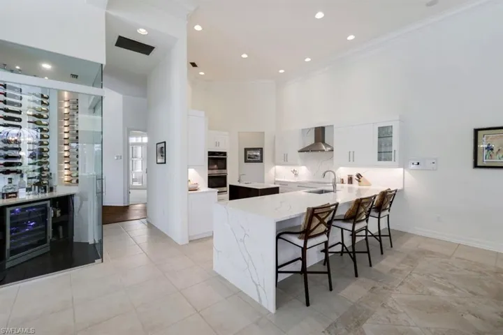 Kitchen featuring kitchen peninsula, white cabinets, beverage cooler, a towering ceiling, and wall chimney exhaust hood