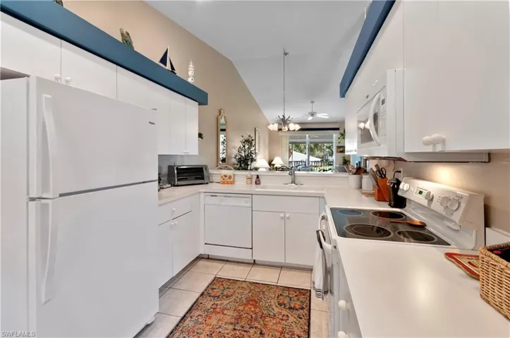Kitchen featuring white cabinetry, white appliances, decorative light fixtures, and sink