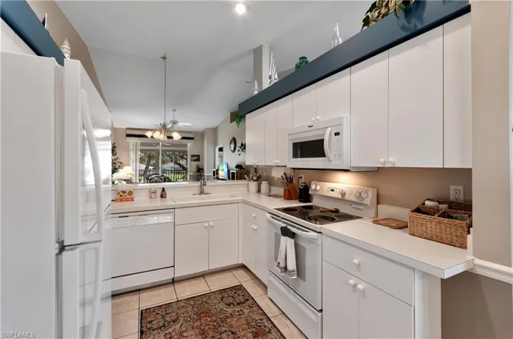 Kitchen featuring sink, light tile patterned floors, white cabinets, and white appliances