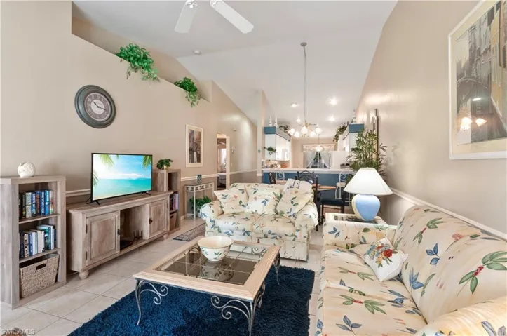 Living room featuring high vaulted ceiling, ceiling fan with notable chandelier, and light tile patterned floors