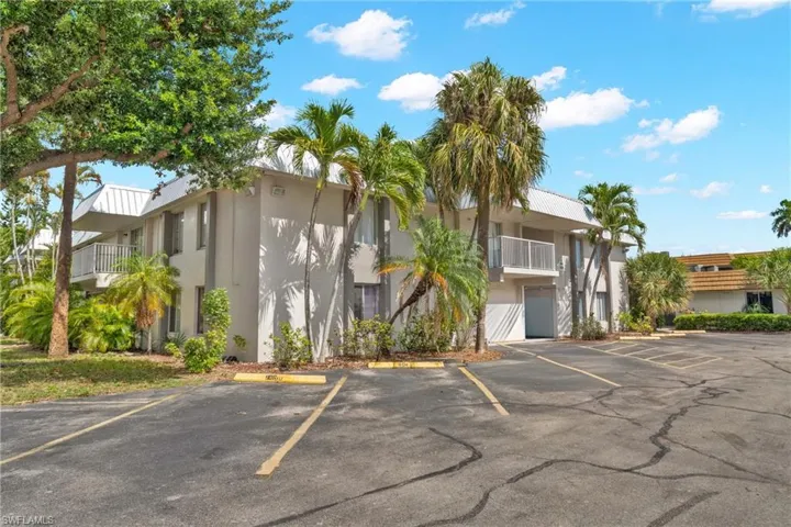 Two-story stucco building featuring multiple balconies with white railings, mature palm trees, and established landscaping