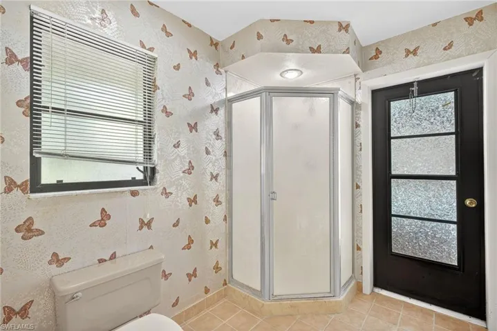Bathroom with wallpapered walls, plenty of natural light, a shower stall, and light tile patterned flooring