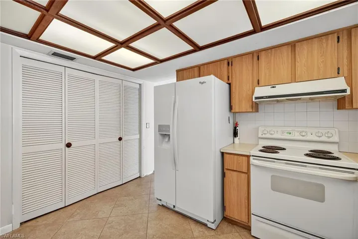 Kitchen featuring white appliances, brown cabinetry, light countertops, exhaust hood, and tasteful backsplash