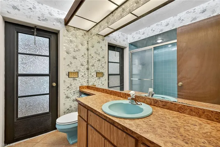 Bathroom with wallpapered walls, a shower stall, vanity, light tile patterned flooring, and healthy amount of natural light