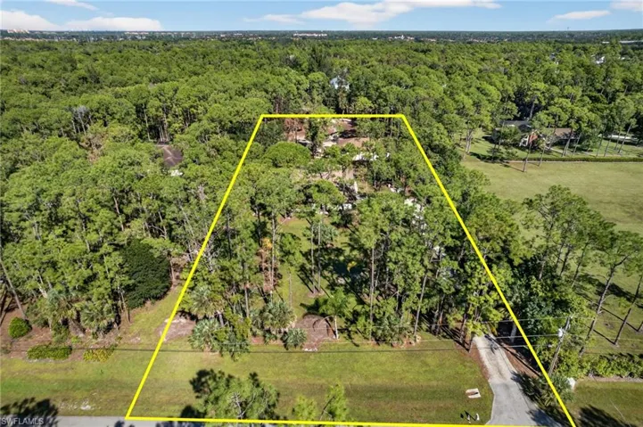 Aerial view of property and surrounding area featuring property parcel outlined and a heavily wooded area