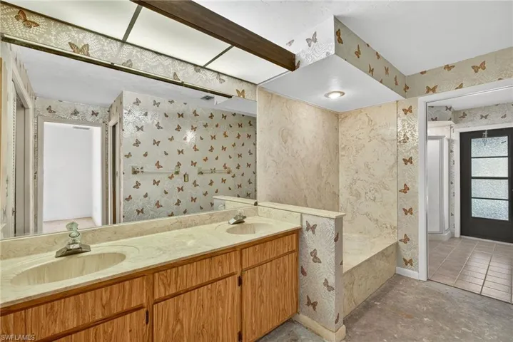 Bathroom featuring wallpapered walls, double vanity, a garden tub, and concrete floors