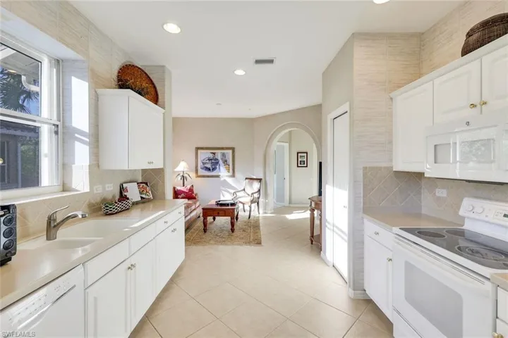 Kitchen featuring white appliances, white cabinets, arched walkways, decorative backsplash, and recessed lighting