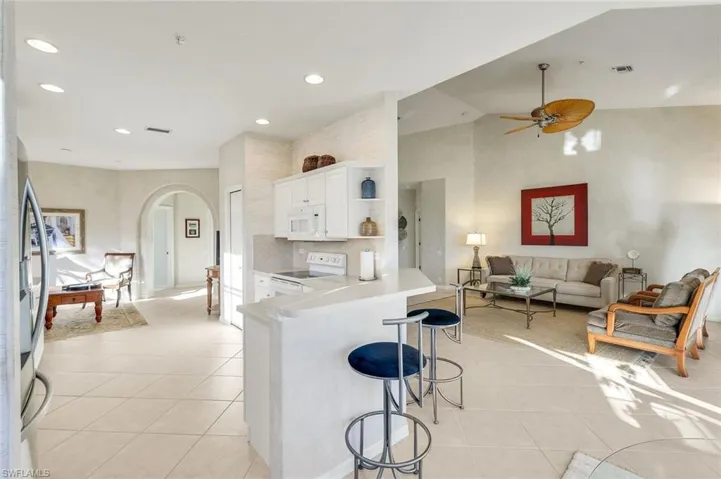 Kitchen featuring arched walkways, white appliances, open shelves, a breakfast bar area, and backsplash