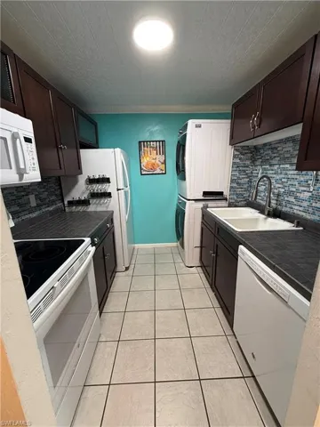 Galley kitchen featuring dark wood cabinetry, a mosaic tile backsplash, and light tile flooring