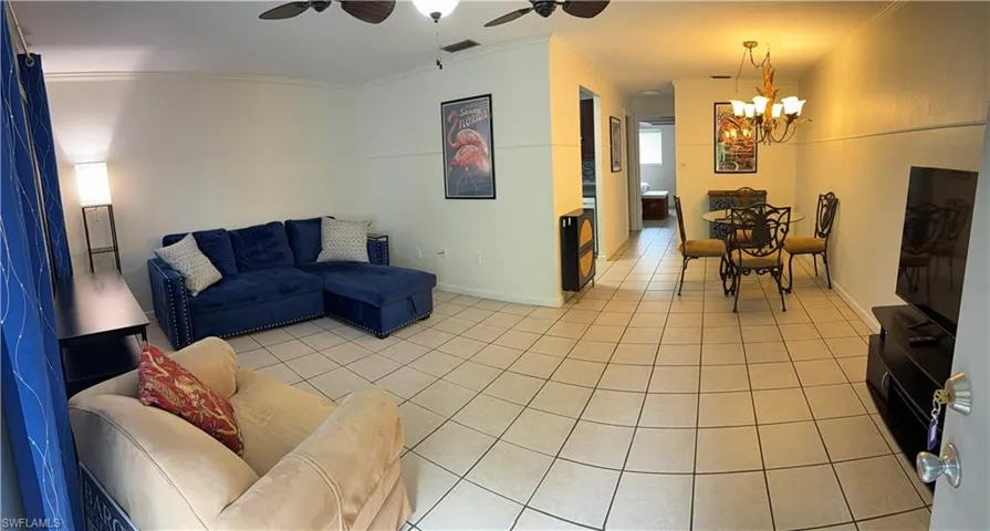 Open-concept living area with tile flooring throughout, featuring crown molding, a ceiling fan, and a chandelier-style light fixture